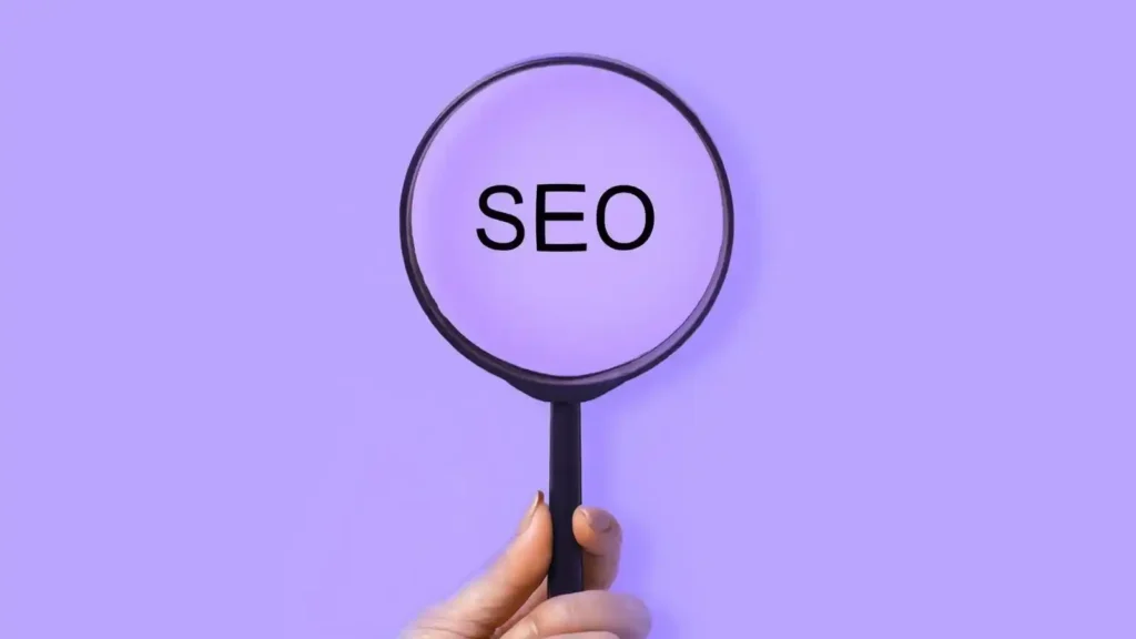 Ecommerce: How to build an online store with technology, user experience and artificial intelligence Mano sosteniendo una lupa que amplifica la palabra "SEO" sobre un fondo morado, simbolizando la optimización para motores de búsqueda en comercio electrónico.