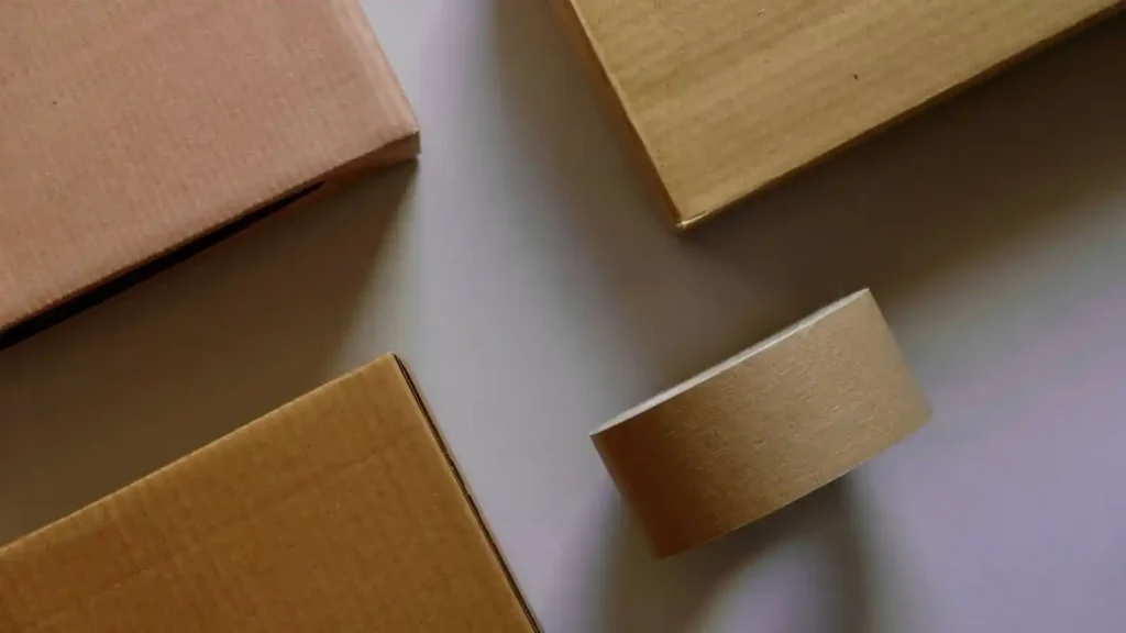 Ecommerce: How to build an online store with technology, user experience and artificial intelligence Cajas de cartón y cinta adhesiva sobre superficie blanca, representando el embalaje y logística en comercio electrónico.