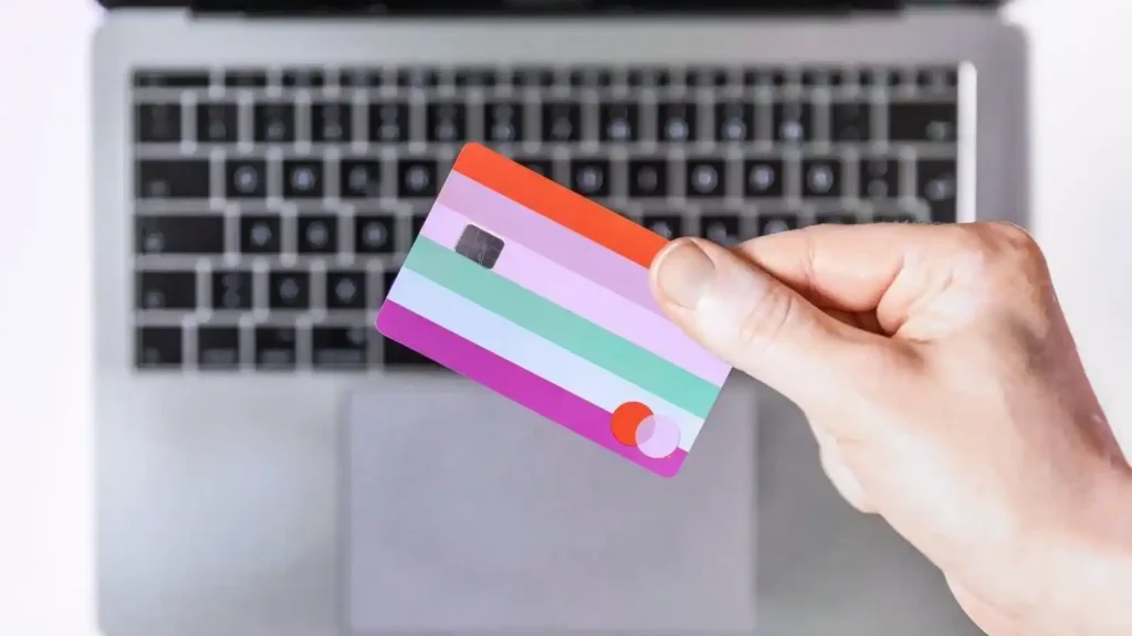 Ecommerce: How to build an online store with technology, user experience and artificial intelligence Mano sosteniendo una tarjeta de crédito colorida sobre un teclado de laptop, representando el proceso de pago en el comercio electrónico.