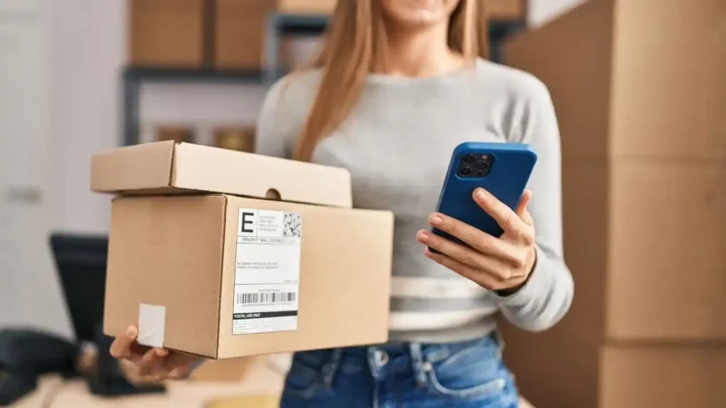 Ecommerce: How to build an online store with technology, user experience and artificial intelligence Mujer sosteniendo dos cajas de envío y un teléfono móvil, simbolizando la integración de compras en e-commerce y la importancia de la sostenibilidad en el comercio online.