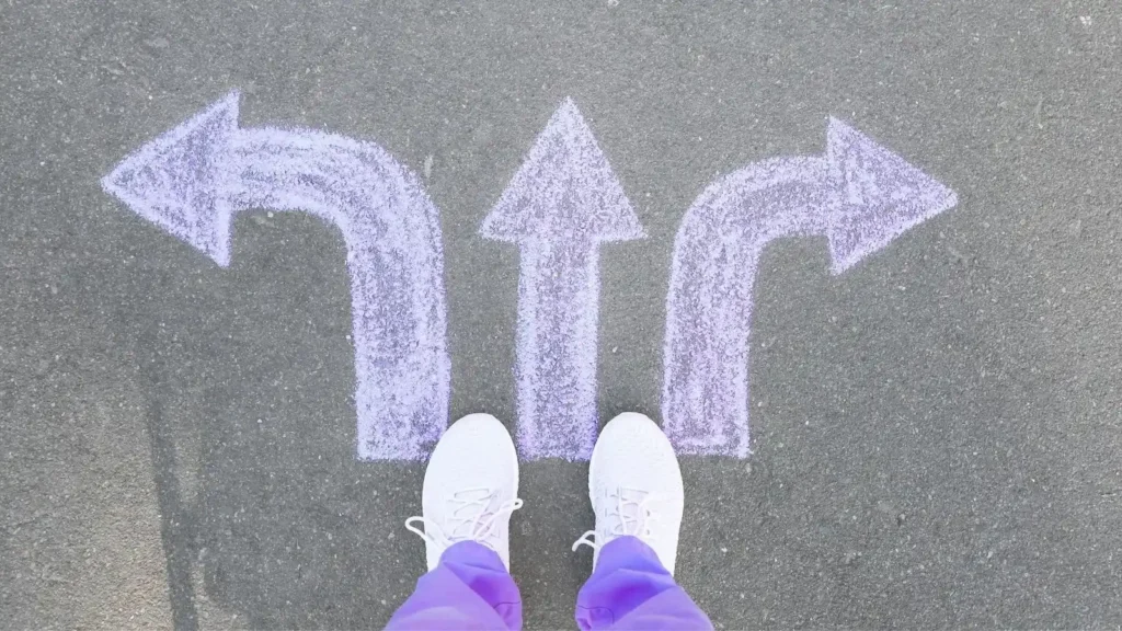 Ecommerce: How to build an online store with technology, user experience and artificial intelligence Zapatos blancos de pie sobre un pavimento con flechas de tiza indicando direcciones, simbolizando decisiones en el contexto del crecimiento del comercio electrónico y la elección de plataformas como Shopify y WooCommerce.